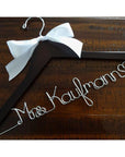 Dark black wooden hanger with a white satin bow and silver hook. Personalized base wire shaped with the name "Mrs. Kaufmann" and a heart.