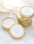 Your design here custom wedding favor candle shown 4 gold tins shown, 3 stacked up, one opened showing a white candle inside, they have a white round label with the words your design here in black lettering.