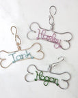 Personalized Dog ornament image that shows 3 of them 2 with a dog bone shaped outline, silver aluminum wire with the names Harlet in light pink and Hogan in green. Then one in dog bone shaped in gold aluminum wire with the name tank in ice blue. All of them in a white background.