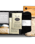 Savon Parfume Extra Pur soap in a gray wrapper. honey in a clear square jar with a silver lid, two 'No. 15' Steven Smith Teamaker packets, black 'foxblossom' cozy socks, and a Christina Maser Pantry chicken soup mixture, in a black 'foxblossom' box with black paper shread