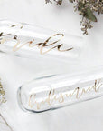 Two personalized champagne flutes, read "bride" and "bridesmaid" in mirrored gold script.