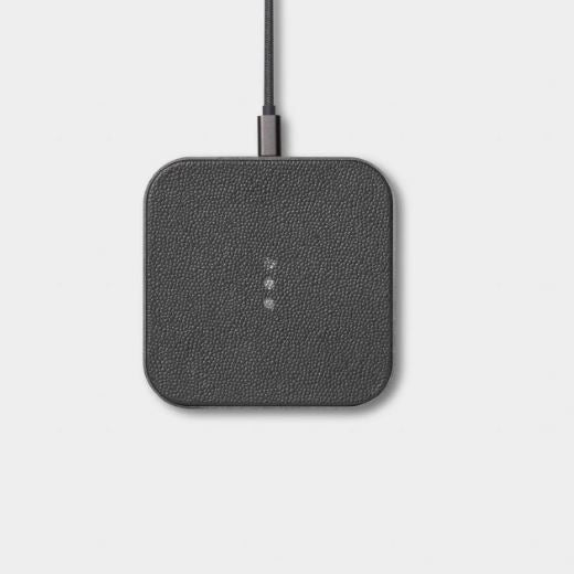 A dark gray square wireless charging pad with rounded corners and a textured leather-like finish, shown with a black cable connected at the top against a light gray background.