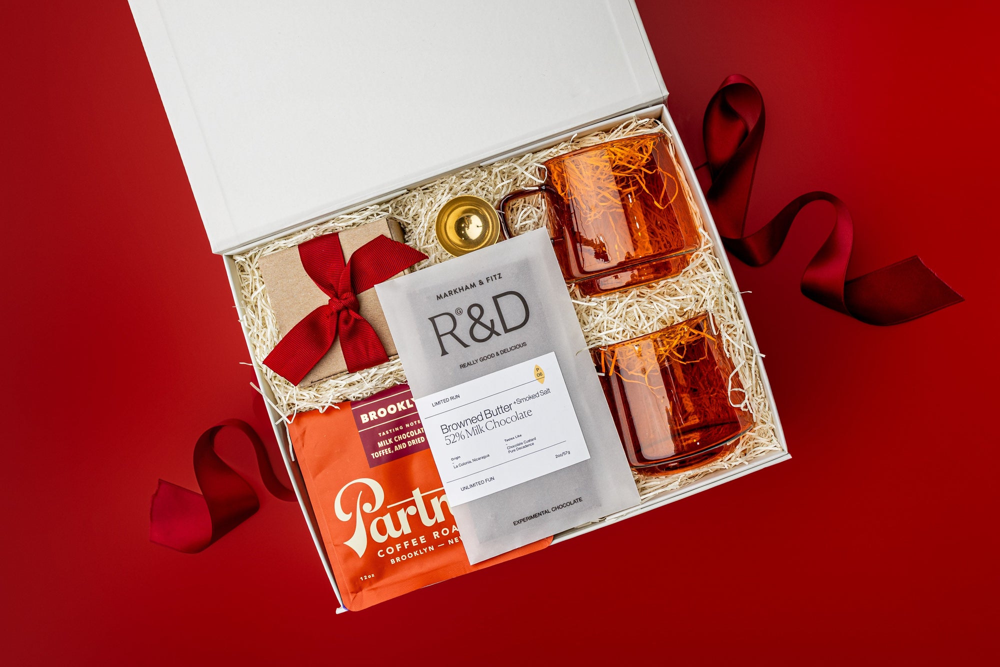 Christmas gift box with coffee, mugs, chocolate bar and caramels on red background.