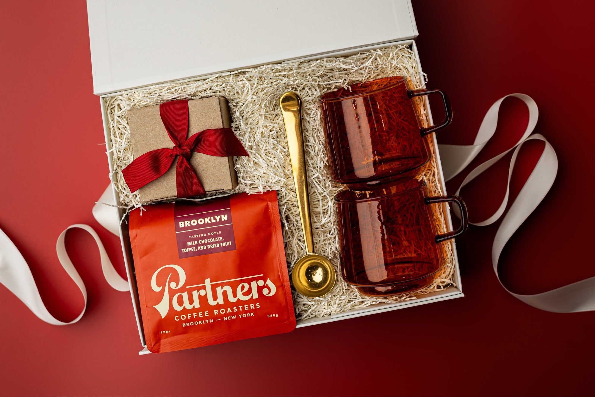 Gift set with coffee bags, mugs, and a spoon on a red background