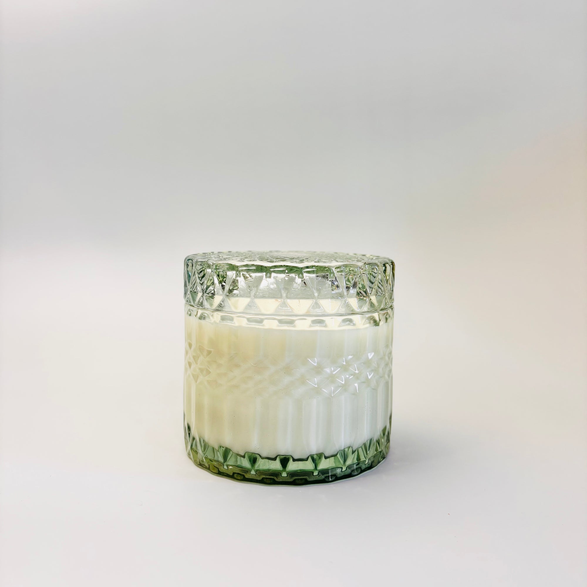 Amber & Moss Candle is featured in its  green trinket glass jar, on a white background.