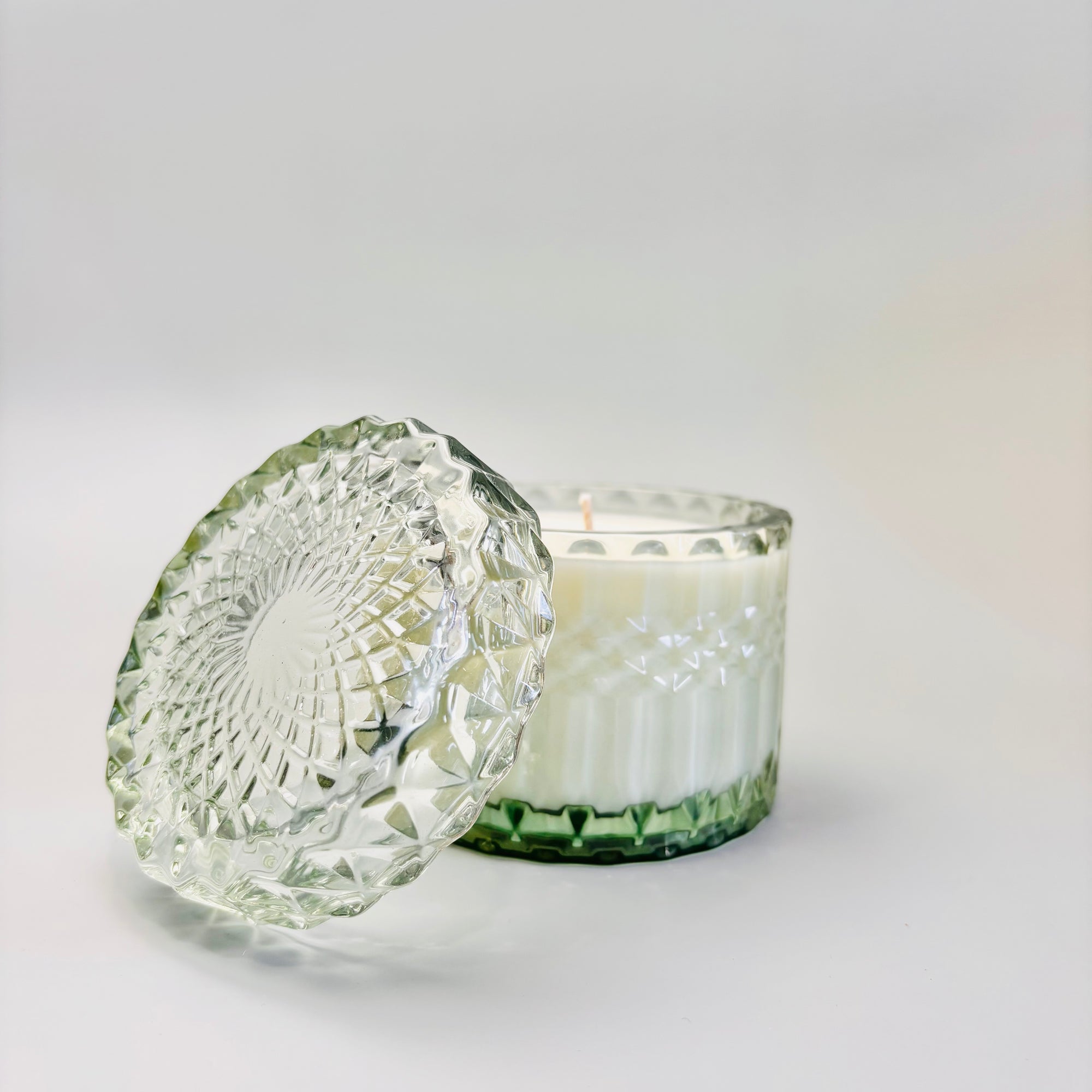 Amber & Moss Candle is featured in its green trinket glass jar, with its lid on a white background.