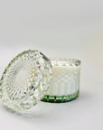Amber & Moss Candle is featured in its green trinket glass jar, with its lid on a white background.