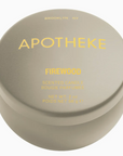 Apotheke Firewood Mini Candle in a small, round metal tin with a silver lid, labeled ‘Firewood,’ showing creamy white wax inside.