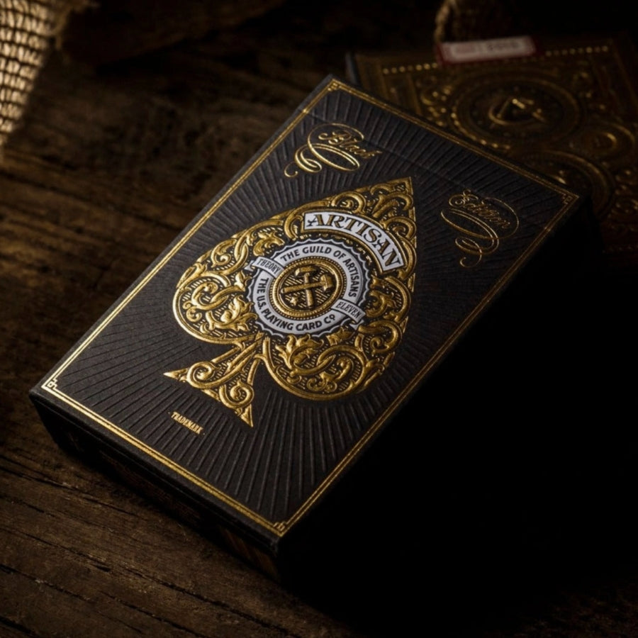Black and gold playing card box with intricate design on a wooden surface