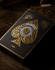 Black and gold playing card box with intricate design on a wooden surface
