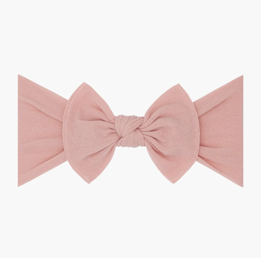 A dusty pink fabric headband with a large bow and knotted center, shown flat against a plain white background.