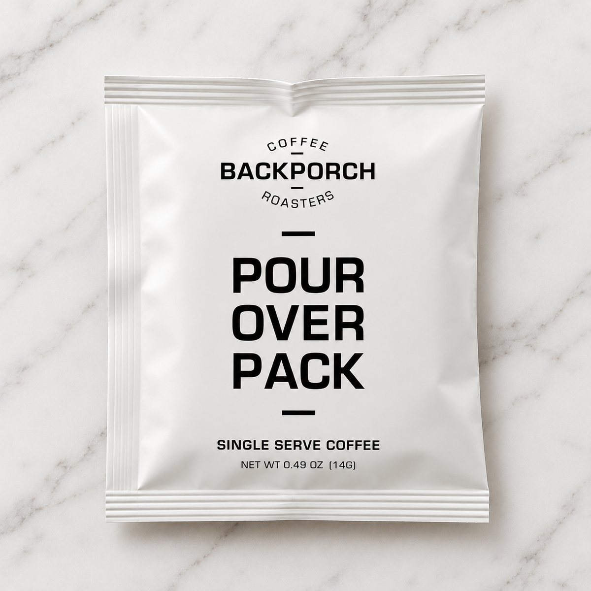 A single white pour-over coffee packet with black text reading 'COFFEE BACKPORCH ROASTERS POUR OVER PACK SINGLE SERVE COFFEE' on a light marble surface.