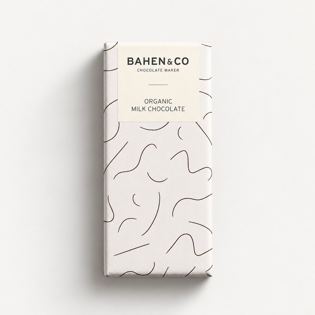 A wrapped chocolate bar package from Bahen & Co, featuring a minimalist cream-colored wrapper with black abstract line patterns and a cream label at the top that reads 'BAHEN&CO CHOCOLATE MAKER' and 'ORGANIC MILK CHOCOLATE'.