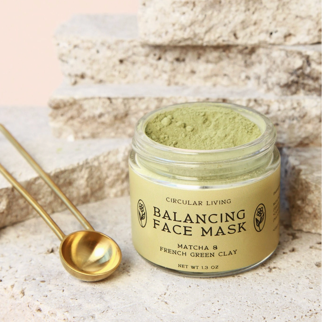 Balancing face mask jar with gold spoon on a textured surface