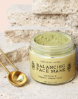 Balancing face mask jar with gold spoon on a textured surface