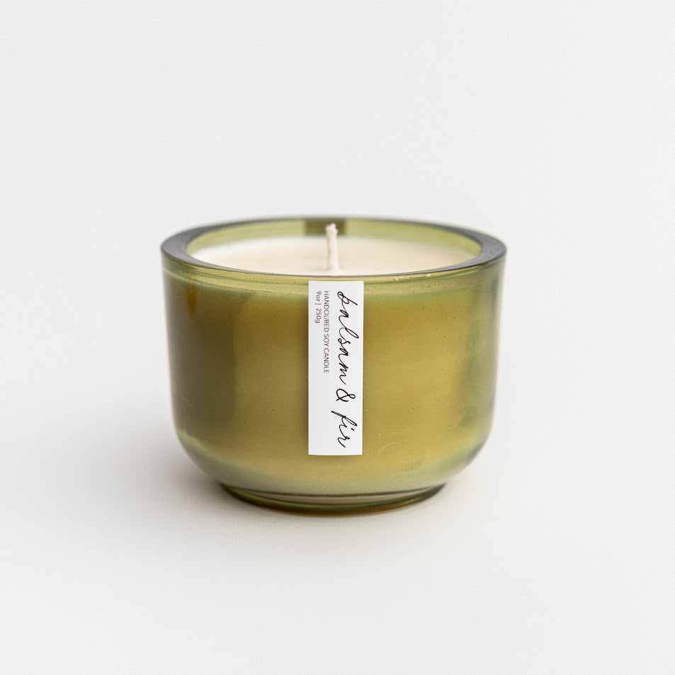 Balsam and fir candle is featured in its green jar with white label with black lettering on a white background. 