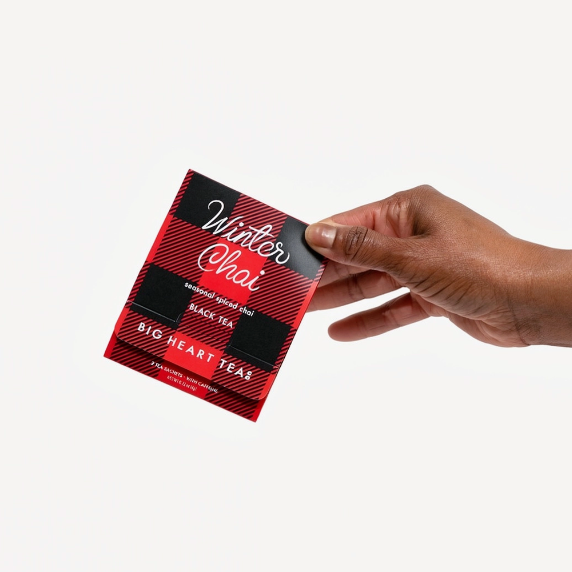 A hand holding a small square tea packet labeled Winter Chai against a plain light gray background.