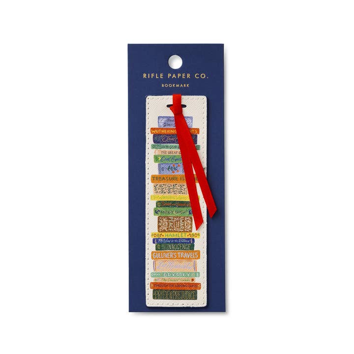 This image displays a Rifle Paper Co. book club bookmark featuring a stack of colorful, illustrated book spines, complete with a red ribbon affixed to a dark blue card, on a white background. 