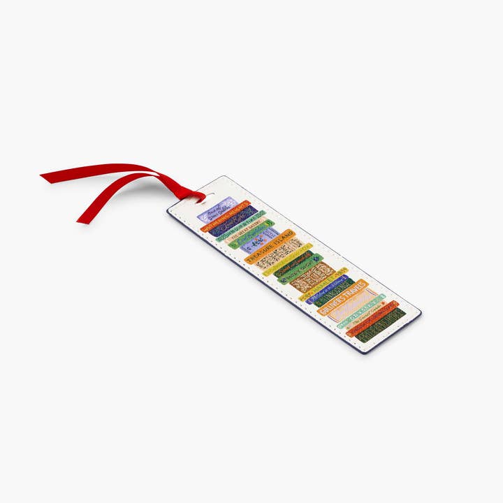 This image displays a Rifle Paper Co. bookmark featuring a stack of colorful, illustrated book spines, complete with a red ribbon affixed to a white background. 