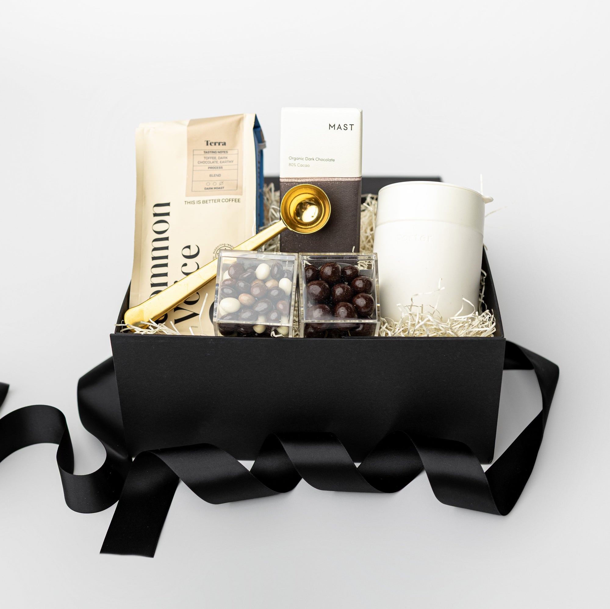 Gift basket with coffee bag and coffee chocolate and caramels, coffee scoop and travel mug with black ribbon on a white background