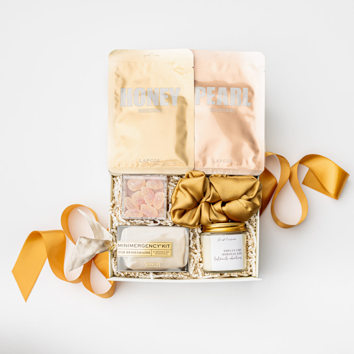 A luxury skincare gift box from Kose, featuring two face masks (Honey and Pearl), a primer, a jar, and a satin bow, arranged in a white box with shredded paper on a white background.