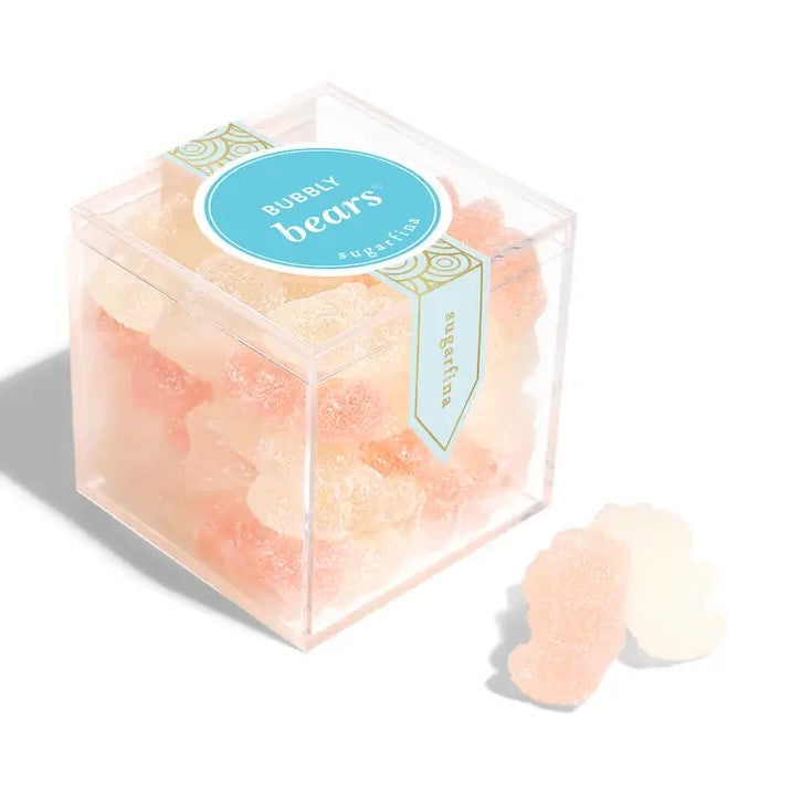 Bubbly bears cube by Sugarfina is fewatured in its square shaped transparente container with blue and gold details label with lettering. In front two of the bubbly bears, on a white background. 
