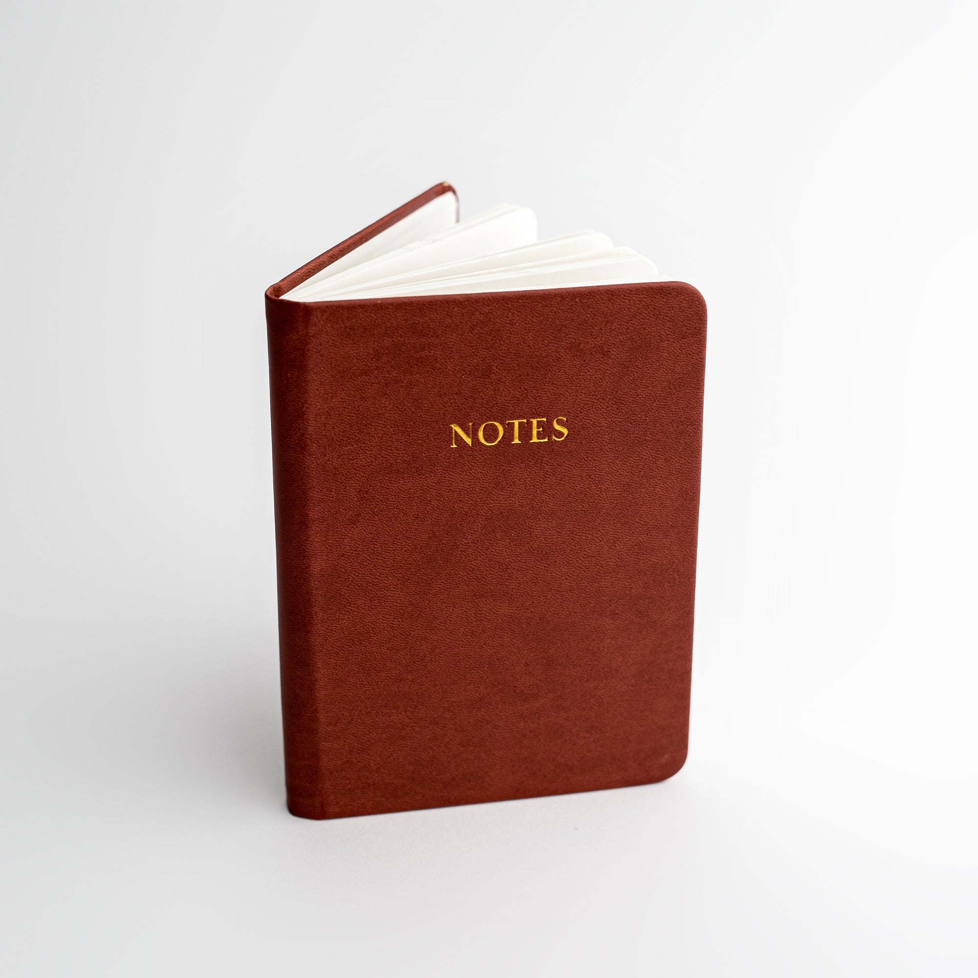 Burgundy pocket softcover notebook featured on a white background.  With Notes in gold in front of it. 