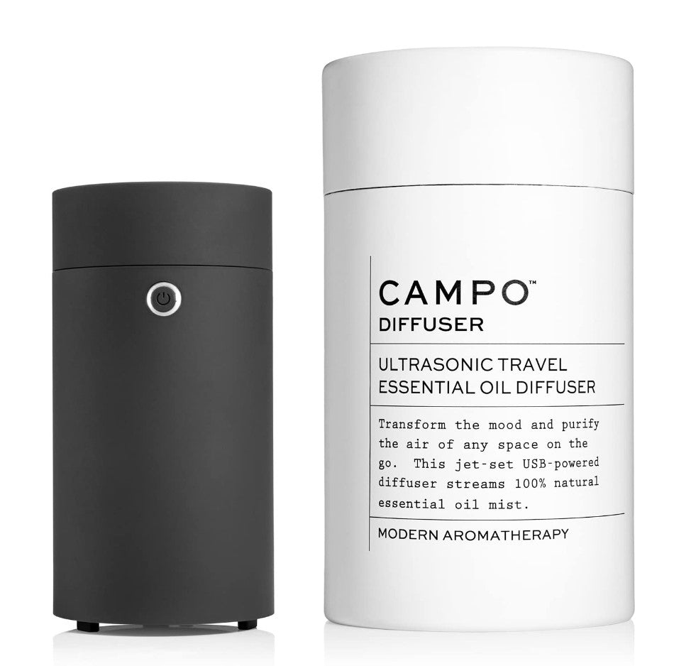 Campo travel essential oil diffuser, featured in its white cylindric container with black lettering with the information. Next to it the diffuser in its cylindrical form and black color.  