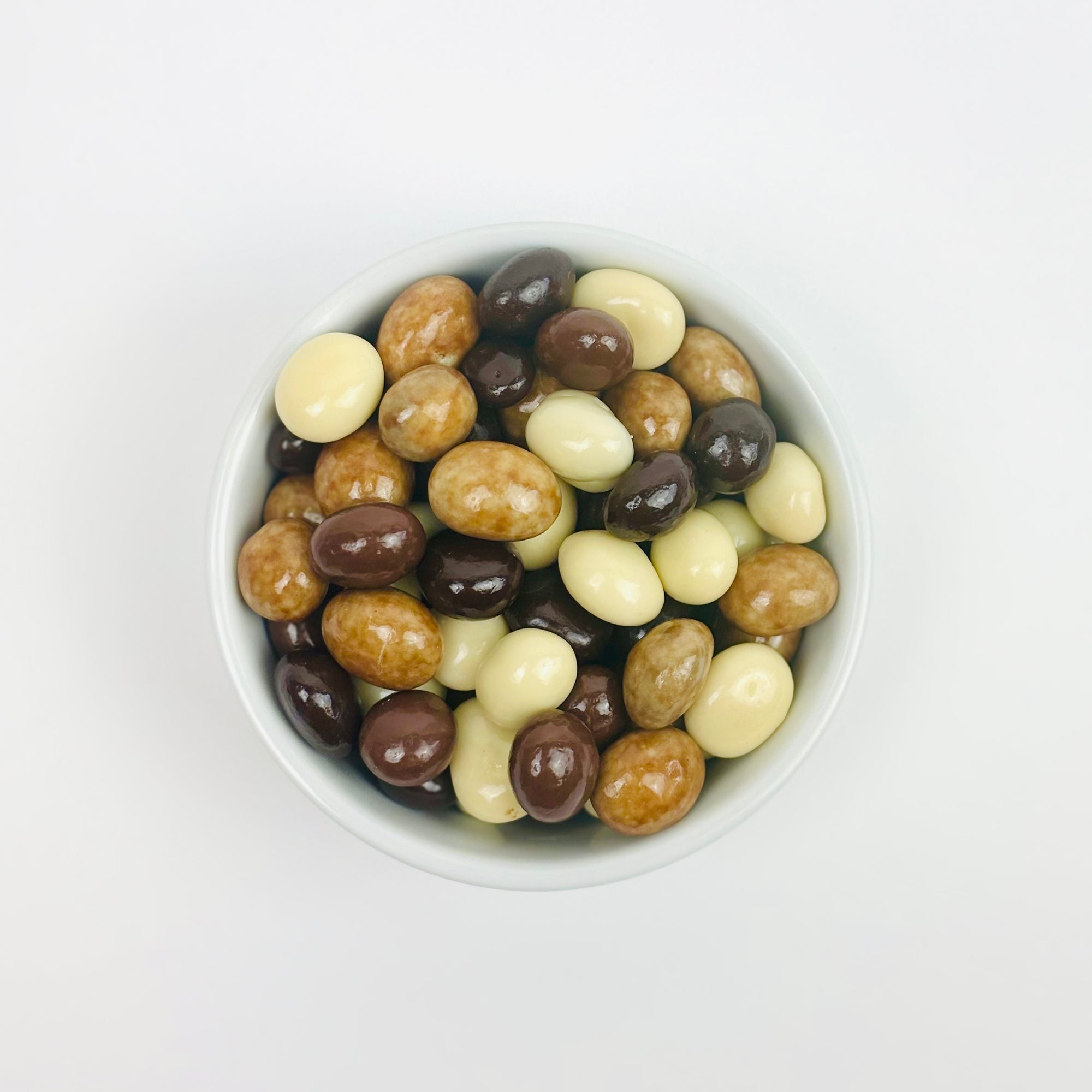 Chocolate covered expresso beans (milk, dark, and white chocolate covering), in a white bowl on a white background.