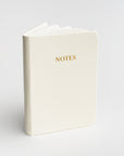 Cream pocket softcover notebook featured on a white background.  With Notes in gold in front of it. 