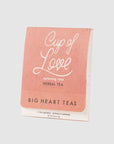 Cup of Love, rose, herbal tea,  the tea package itself, featuring a soft, coral-pink color on the front surface. Large, elegant cursive lettering spells out "Cup of Love" in white, suggesting a comforting and romantic experience. Below that, in a smaller, more straightforward font, are the words "nurturing rose" and "HERBAL TEA." At the bottom, "BIG HEART TEAS" is printed in block capital letters. The package also includes information such as "2 TEA SACHETS - WITHOUT CAFFEINE" and weight.