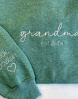 Custom grandma embroidered sweatshirt in color green embroidered in white in the front Grandma Est. 2024 and in the sleeve Elsie and Josiah with a heart emoji on a white background.  