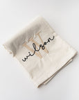 Custom name embroidered white tea towel with W in champagne color and Wilson in black lettering on a white background. 