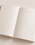 An open lined journal with blank pages, showing a left page labeled 'DATE' and 'WORKING' and a right page labeled 'REFLECTION', photographed on a light beige background.