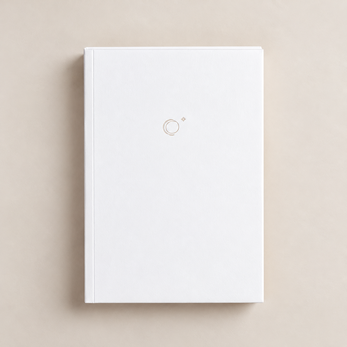 A minimalist white hardcover notebook or journal with a small gold circular logo on the front cover, centered on a warm beige background.