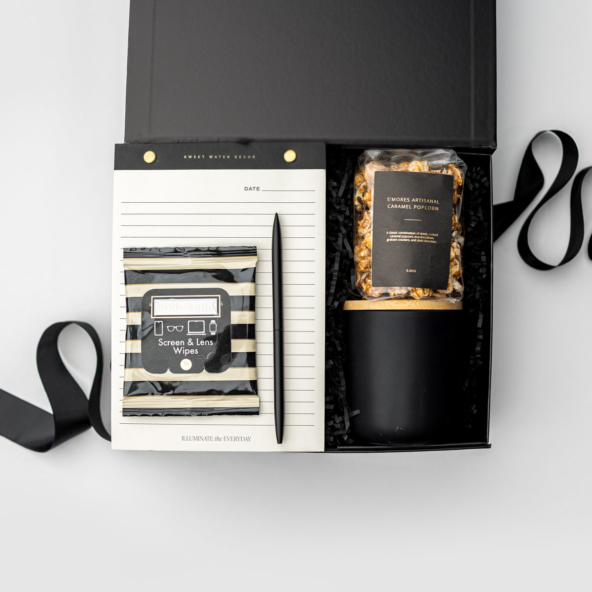 A curated gift box set from Sweet Mash Bakery, featuring a black and white striped soap and lime wipes packet, a black pen, and a jar of caramel popcorn inside a black presentation box with a white lined notepad insert.