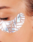 close-up view of a person's eye area with a decorative, iridescent eye patch applied beneath the closed eyelid.

Focused on the upper portion of a person's face, specifically highlighting the eye and the surrounding skin. The eye is closed, with eyelashes visible. Below the eye, a patch is applied; it is an abstract design with a light-reflective, shimmering surface. The frame is tight, centered on the eye area, allowing for a detailed view of skin texture and the texture of the patch. 
