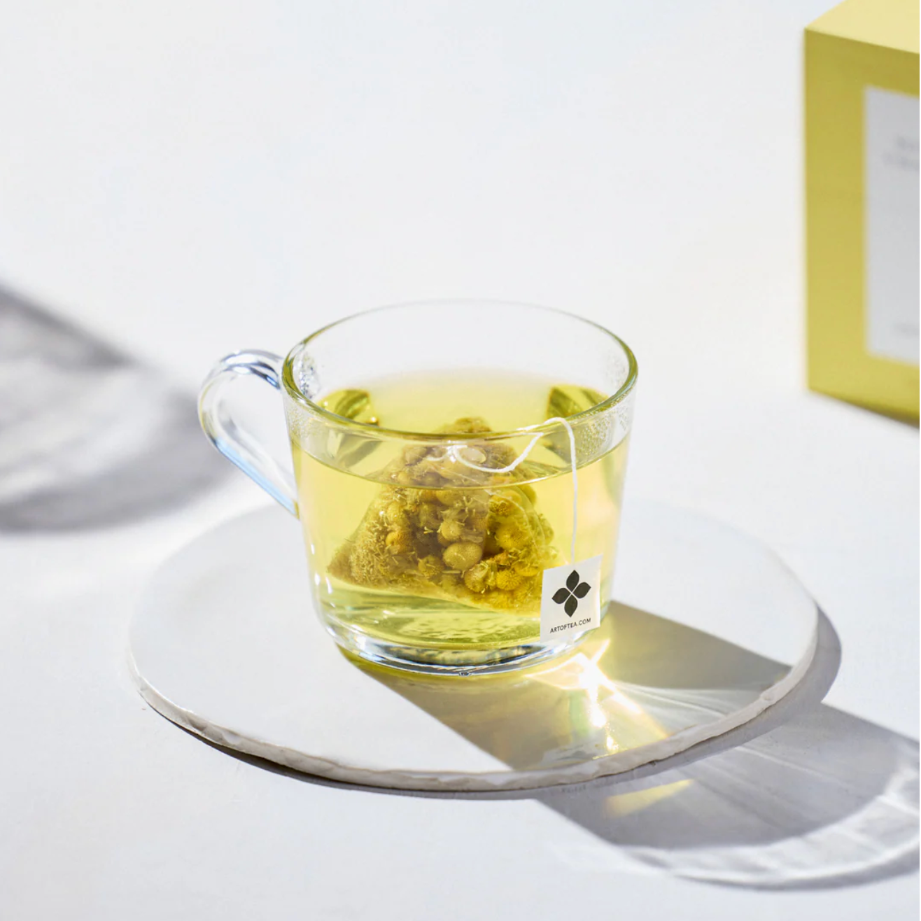 Clear glass mug with green tea and a tea bag on a white surface