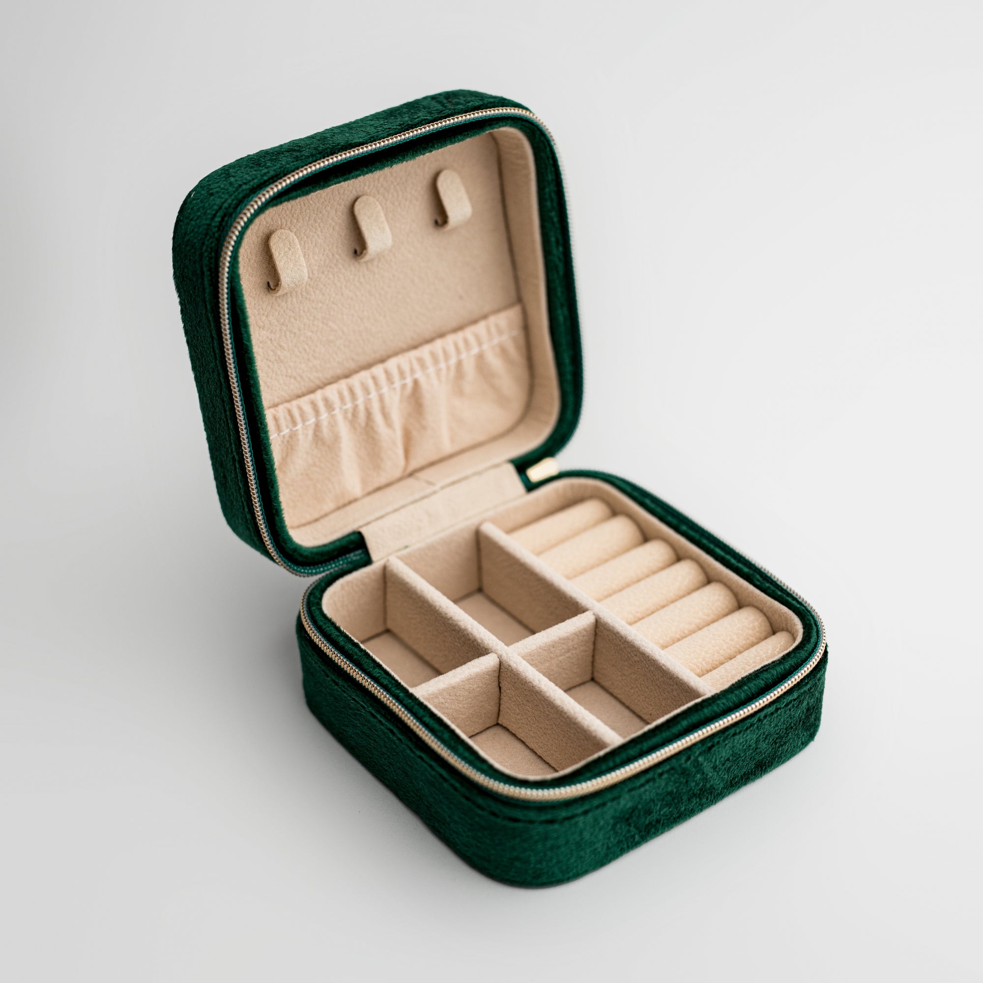 Emerald velvet jewelry box, close-up photograph showcases an emerald velvet jewelry box, opened to display its beige interior compartments and organizers, set against a clean white backdrop.