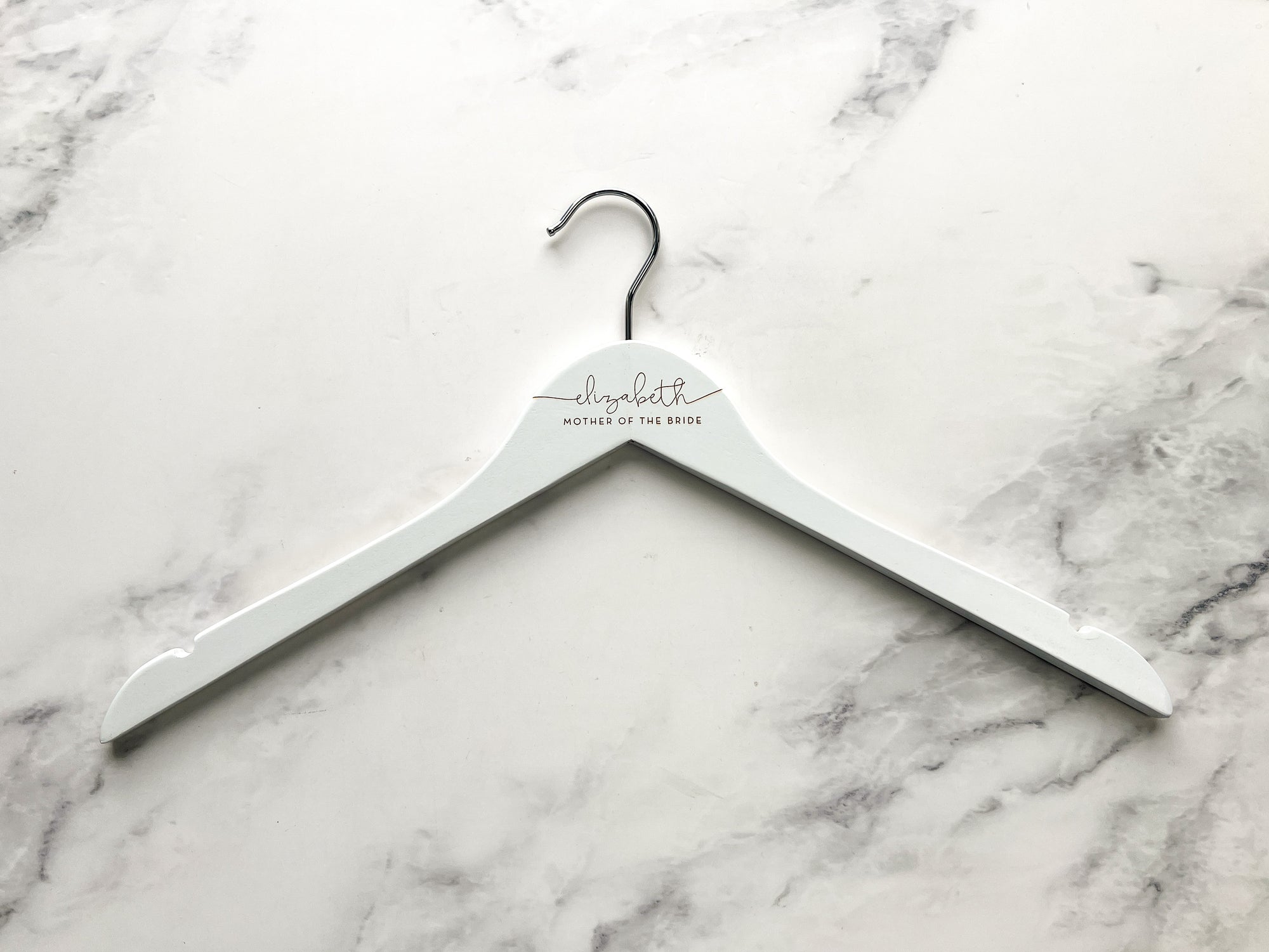 Engraved bride hanger is featured in a white hanger personalized Elizabeth- mother of the bride in a marble like background. 