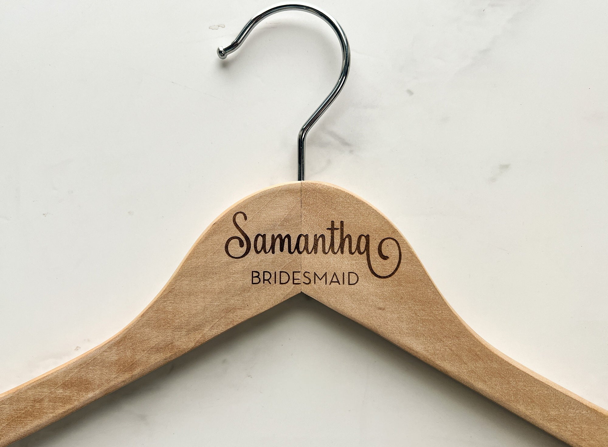 Engraved bride hanger is featured in a natural hanger with silver hook. Engraved Samantha - bridesmaid on a marble-like background.