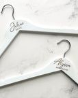 Engraved bride white hangers personalized with Jolene Bride and Alyssa bridesmaid on a marble-like background.