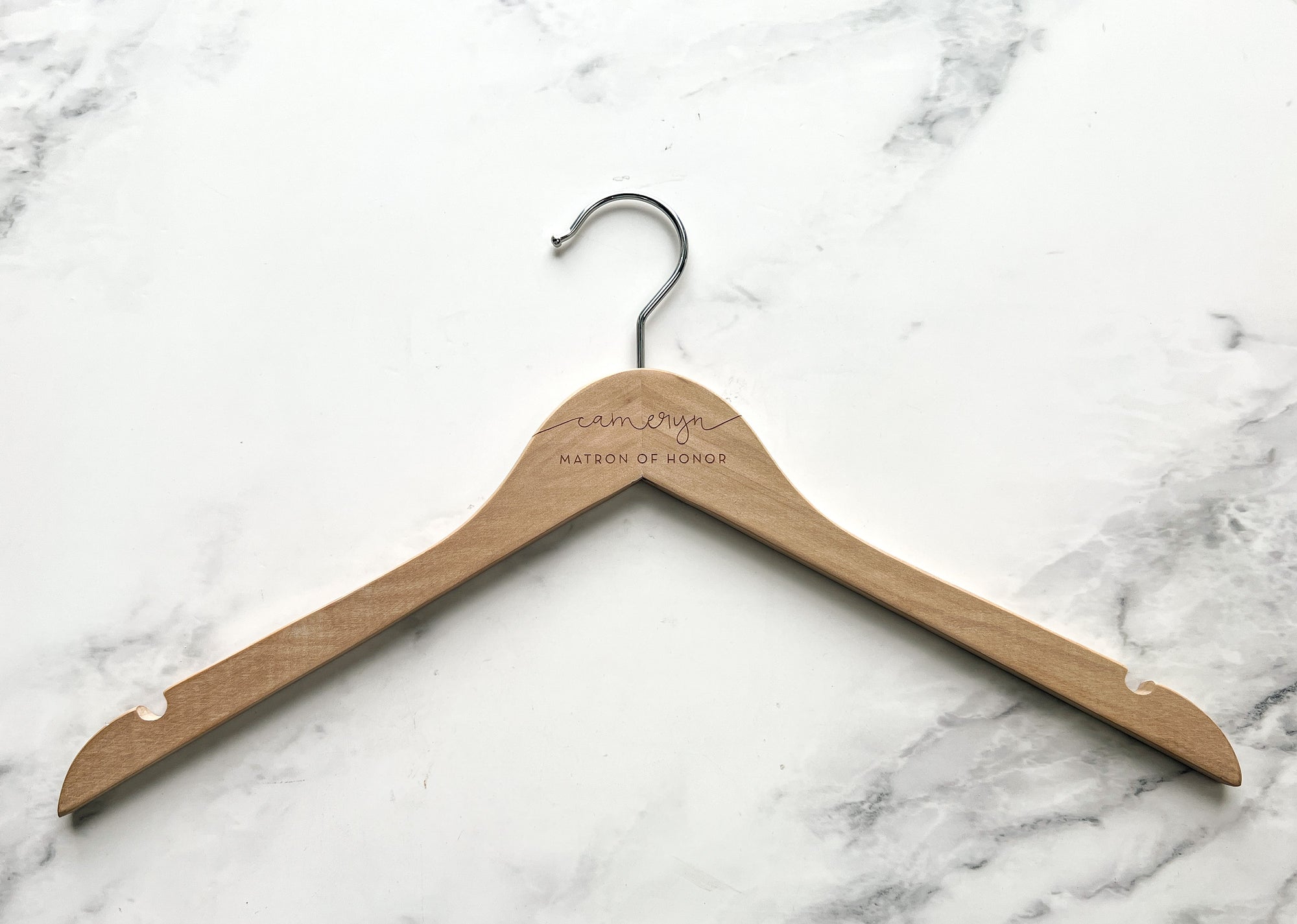 Engraved bride hanger in natural personalized with Cameryn matron of honor on a marble-like background.