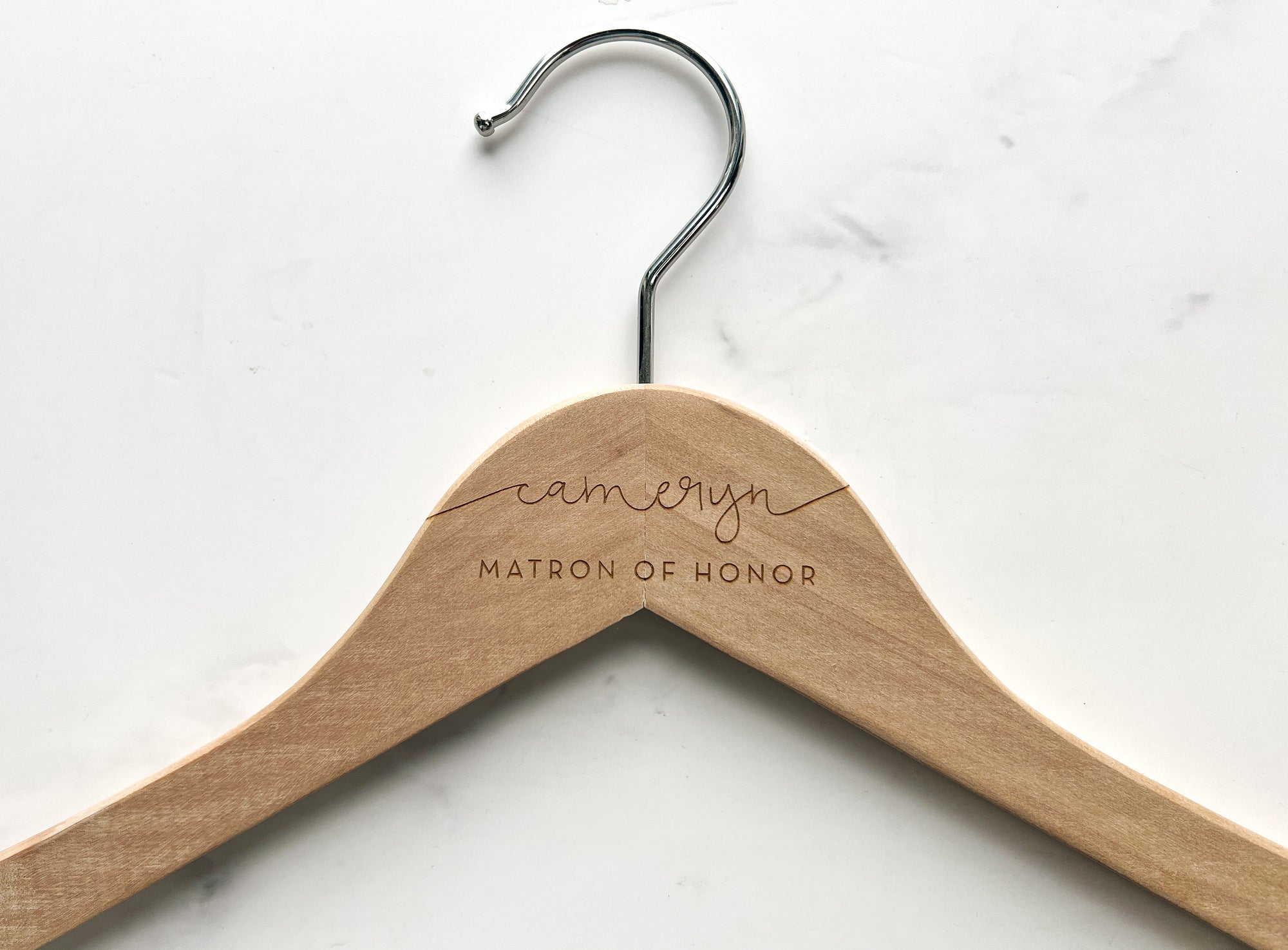 Close up image of natural engraved brie hanger that is personalized Cameryn matron of honor on a marble like background.