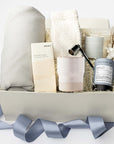 Foxblossom Home gift box featuring an 8 oz. Home Sweet Home cedarwood and vanilla candle, silver candle snuffer, peppermint tea mini tube, cloud socks, speckled stoneware cup, herringbone throw blanket, almond and sea salt chocolate, and a handmade dried floral bouquet, beautifully arranged in gift packaging.