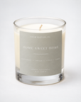 A clear glass jar candle with white wax and a single wick, featuring a light gray label that reads 'FOUR ELEVEN CO. HOME SWEET HOME' on a clean white background.