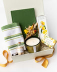 Curated Kitchen Refresh Gift Box with a linen recipe journal, green striped tea towel, gourmet shortbread lemon cookies, white tea scented candle, lemon verbena shea butter and olive oil soap, and a handmade dried floral bundle, packaged for gifting.