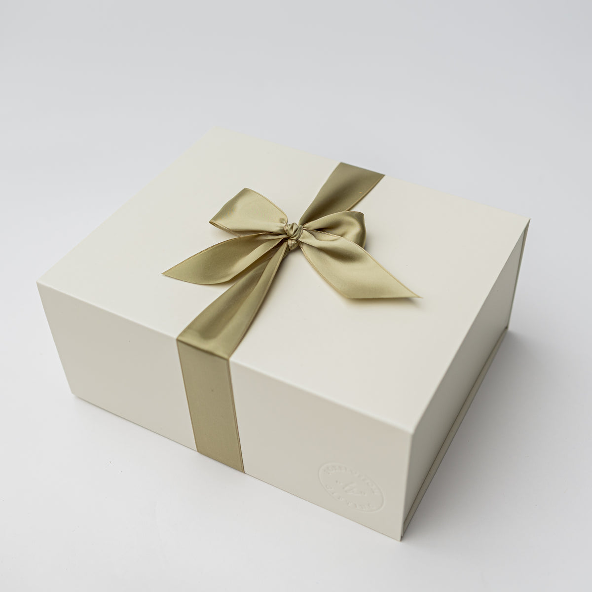 A cream-colored rectangular gift box tied with a satin gold ribbon and bow, photographed on a clean white background.