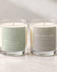 Two lit scented candles in clear glass jars on a light stone surface. The left candle has a pale sage green label reading 'bubbleum Countryside,' and the right candle has a light gray label reading 'FOUR ELEVEN CO.