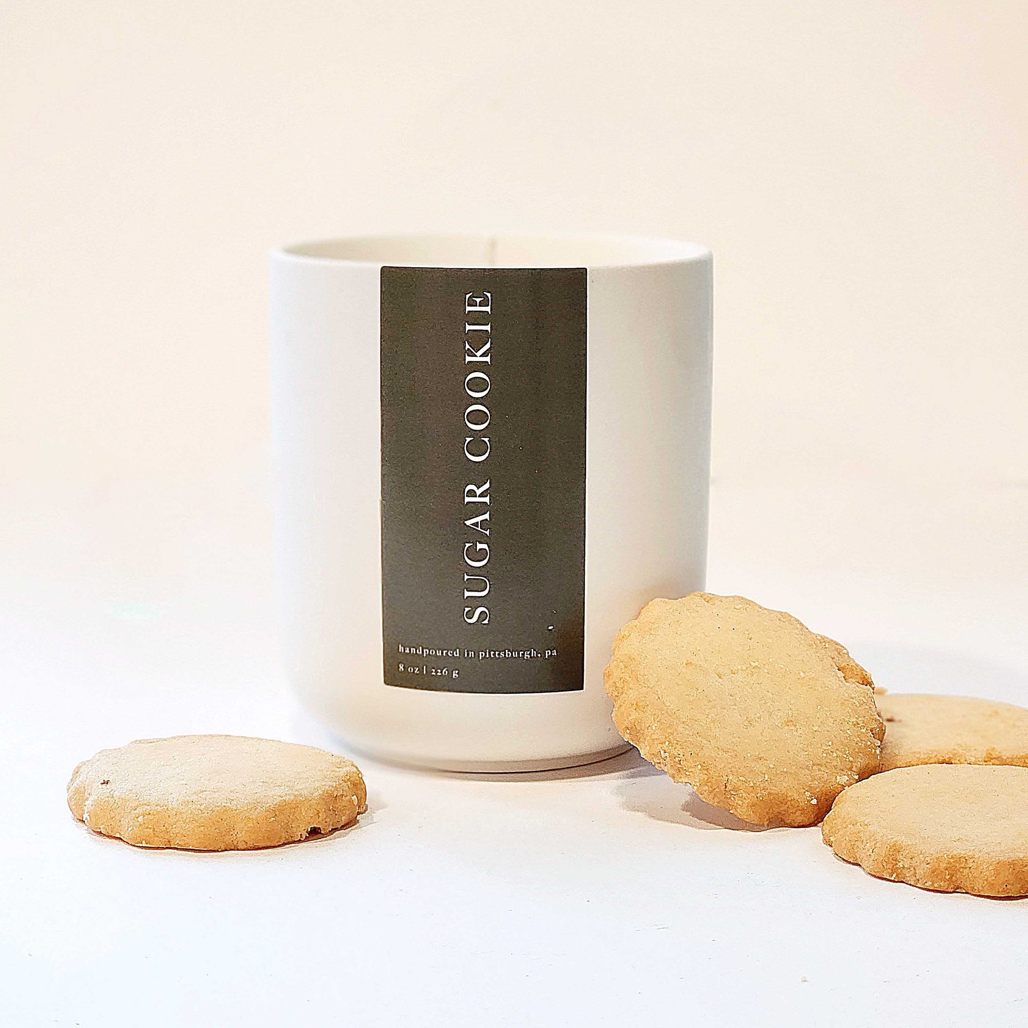 Foxblossom sugar cookie candle is featured in a white ceramic tumbler, 9 oz, surrounded by 4 sugar cookies on a white background. 